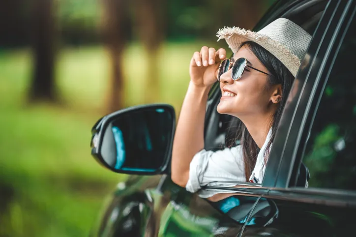 Happy woman hand holding hat outside open window car