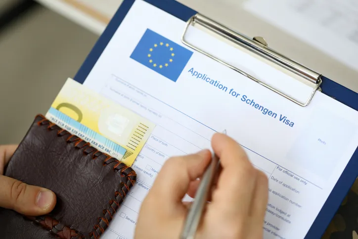 Top view of man filling out documents for Schengen visa while holding money