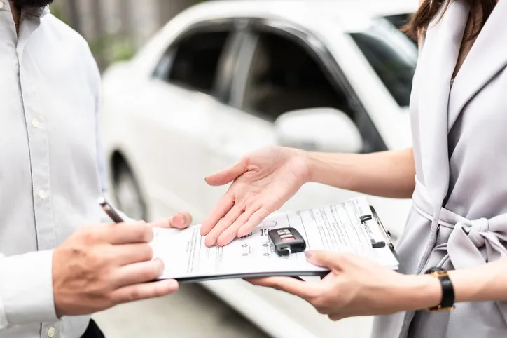 Happy customer with car dealer agent making deal and signing on agreement document contract