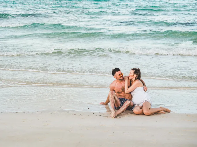 man and pretty woman sitting on the beach with the sea background and looking into the distance