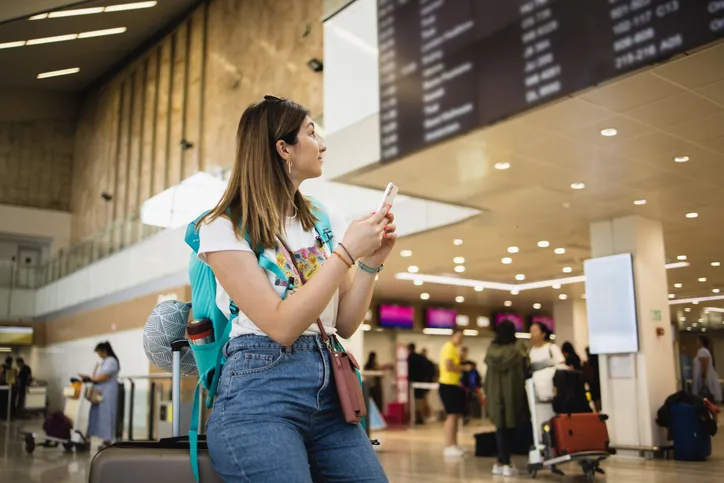 Portrait of a beautiful young woman on vacation waiting on the airport and using smartphone