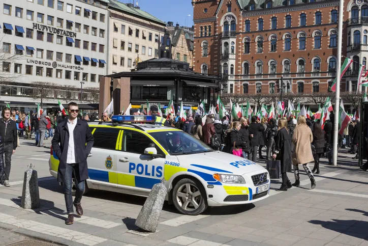 Demonstration for Iran in central Stockholm. In the foreground a polie car watching the demonstration with people with flags moving about. Buildings surrounding Norrmalmstorg. 