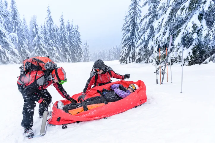 Ski patrol with rescue sled helping injured woman snow forest