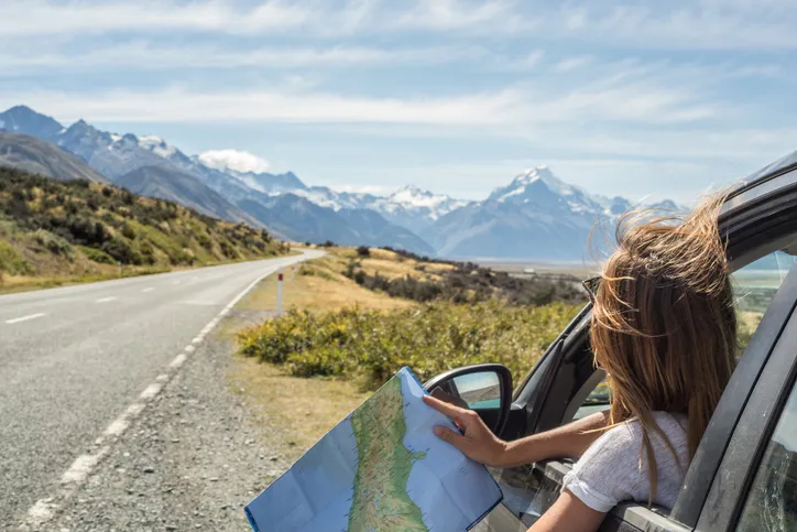 Portrait of a young woman in a car looking at a map for directions.