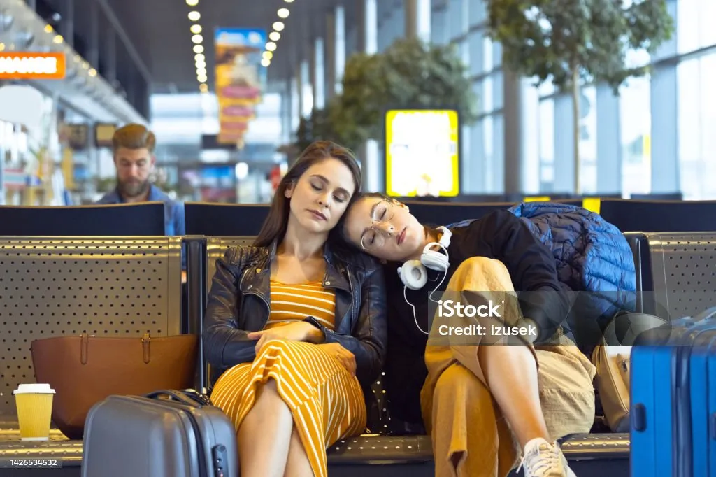 Two young women traveling by plane, waiting for flight and napping in an airport departure area.